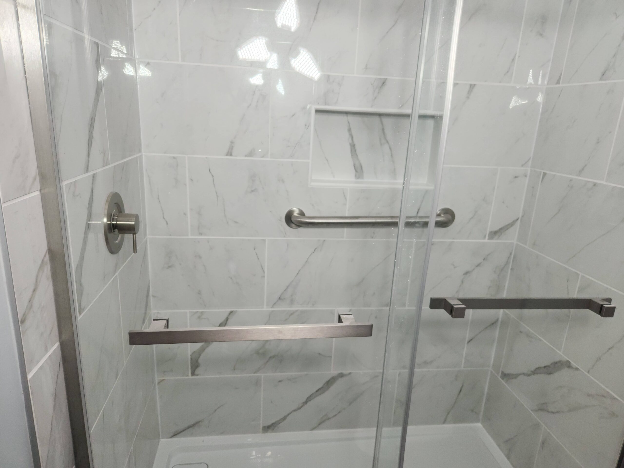Walk in shower with light marble tiles and glass doors