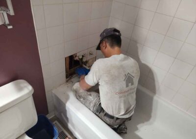 Man sitting in bathtub fixing taps with tiles removed